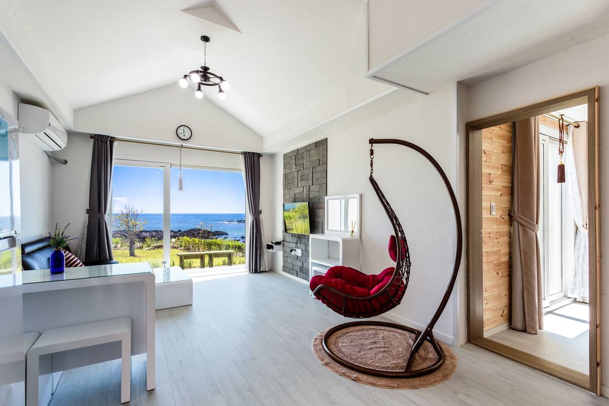 A spacious living area with a hanging chair, a dining table, and a view of the ocean.