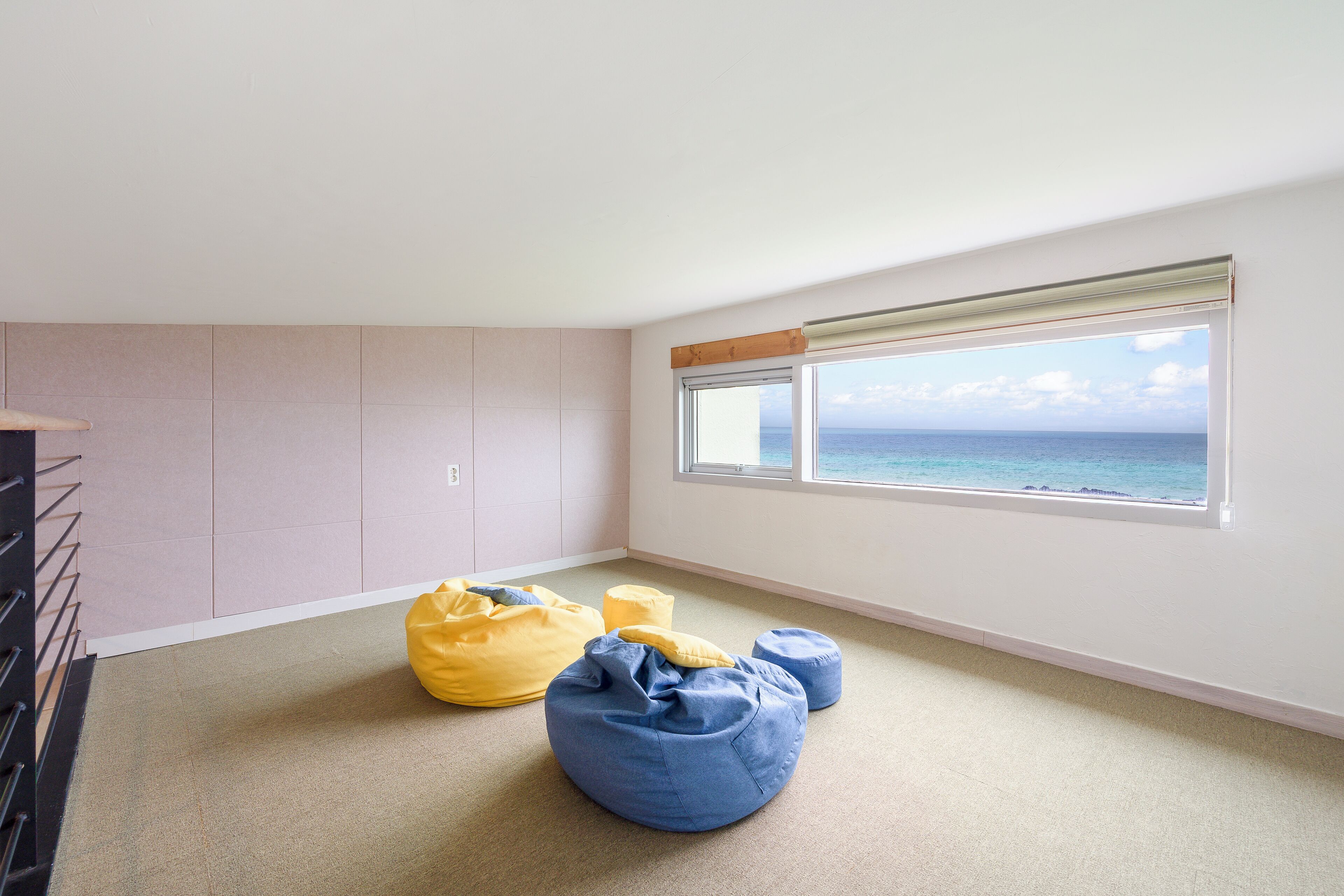 Una habitación con un amplio ventanal, alfombra color beige y dos pufs.