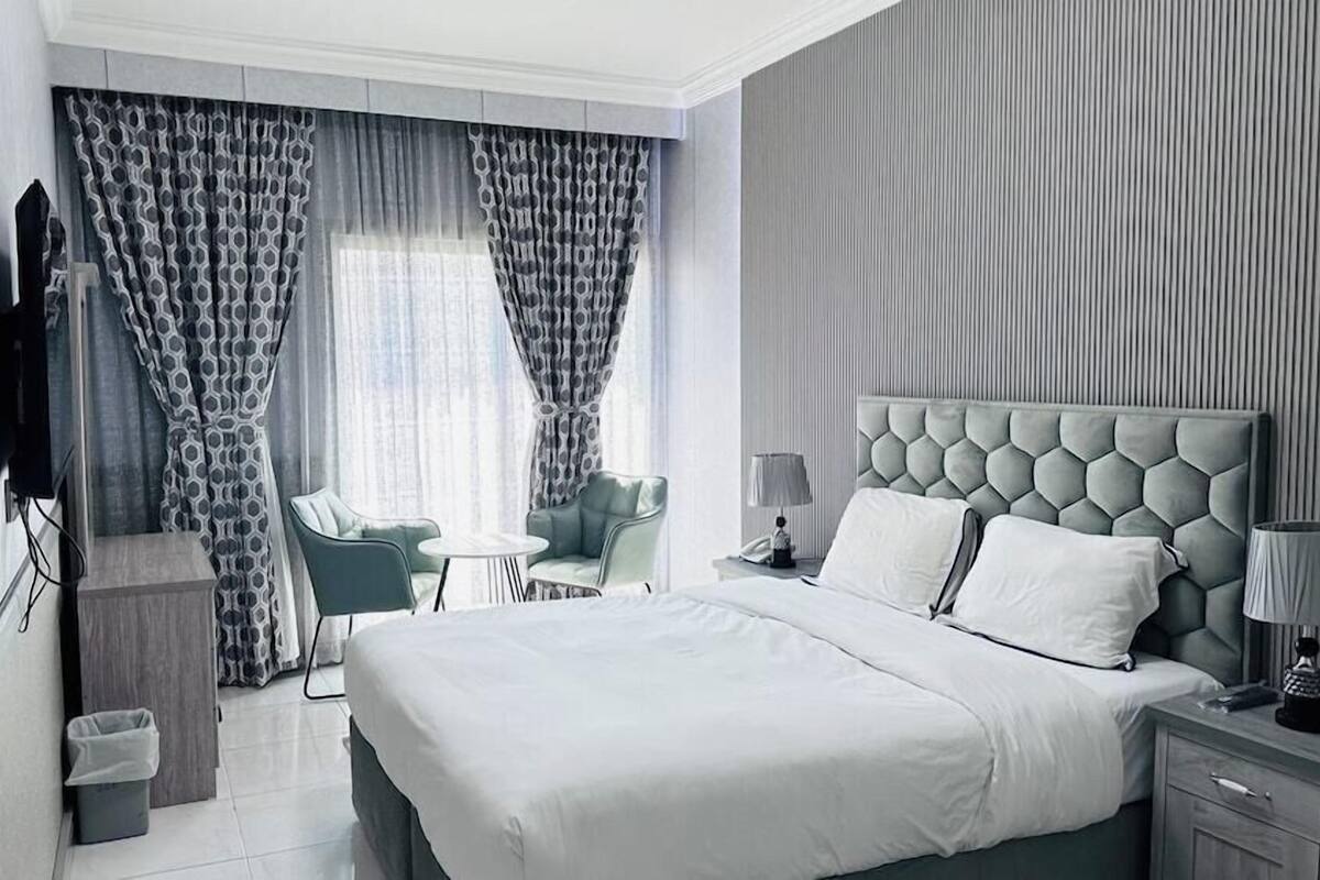 A modern hotel room with a large bed, a desk, a chair, and a TV.