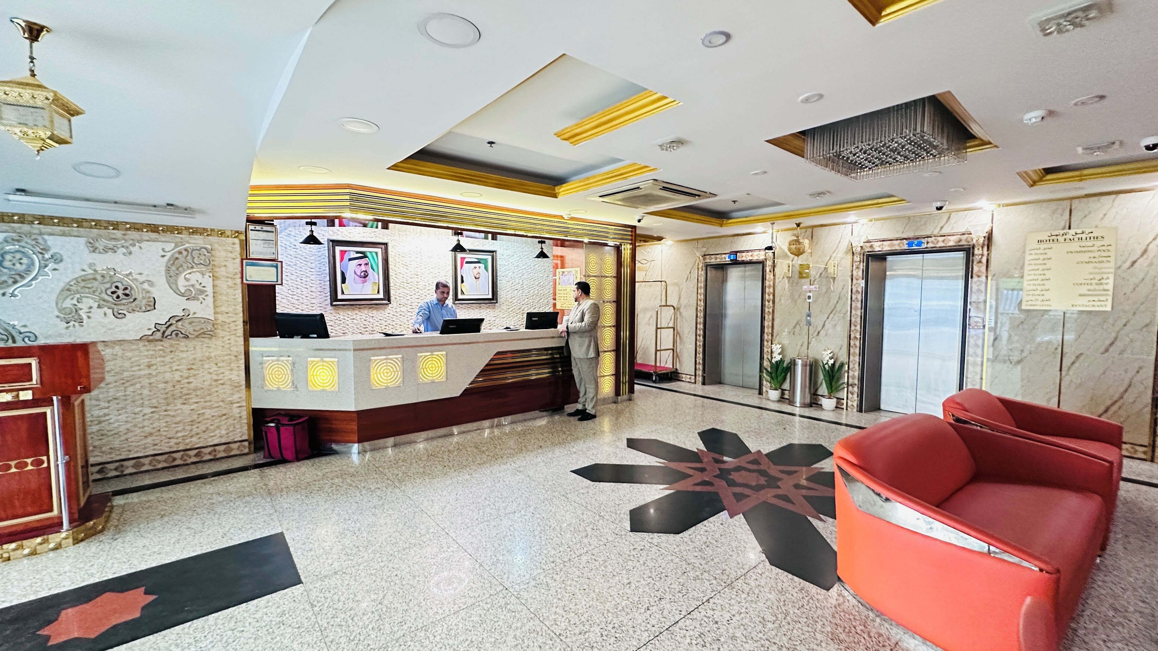 A hotel lobby with a reception desk, elevators, a red chair, and a patterned floor.