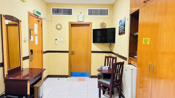 A hotel room with wooden doors, a television mounted on the wall, a safe box sign, and a small table with a chair.