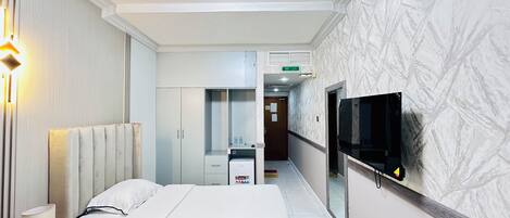 A hotel room with a bed, bedside table, lamp, wardrobe, mirror, and a TV mounted on the wall.