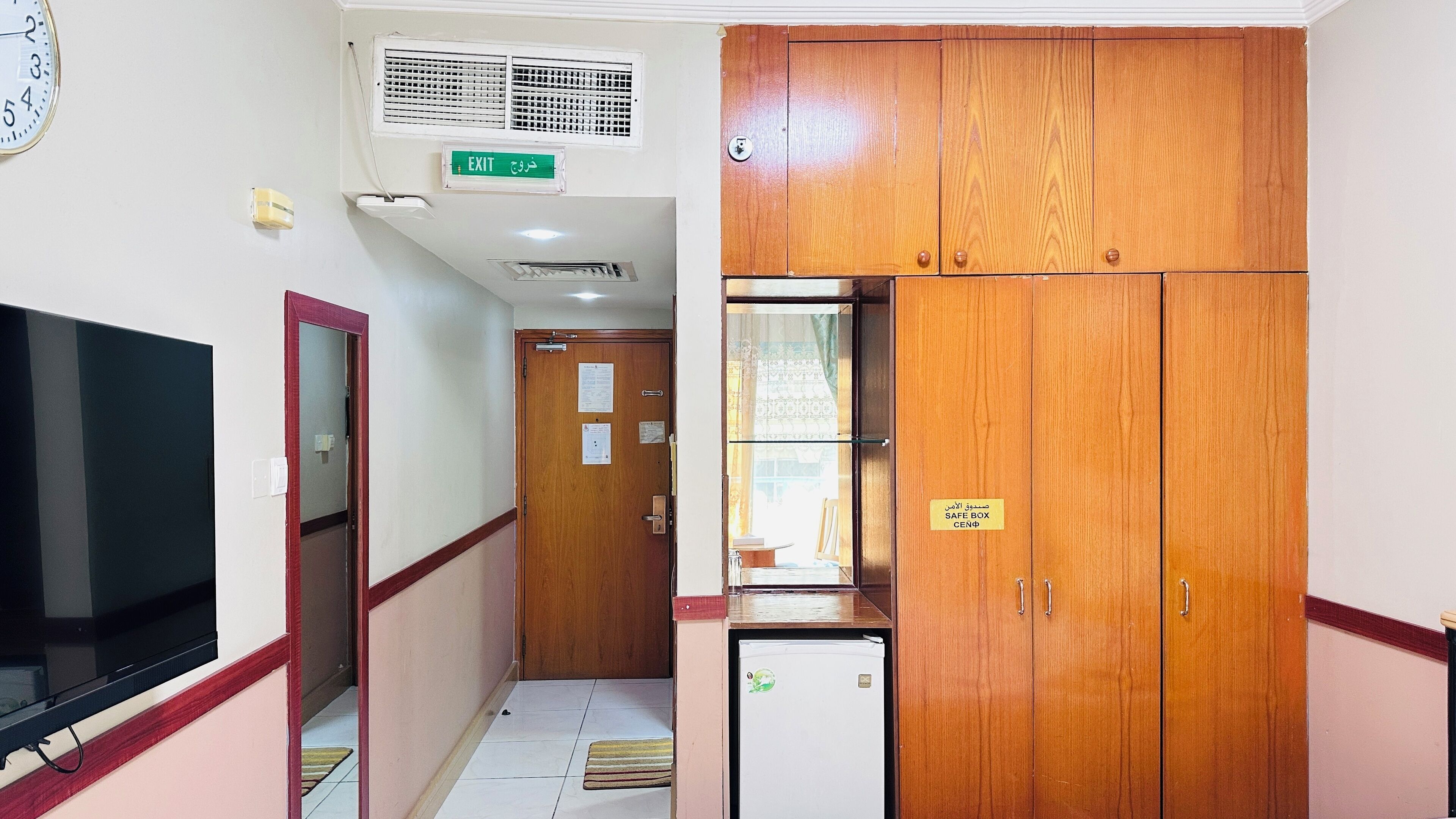 A hallway with a television, an exit sign, a safe box, and wooden cabinets.