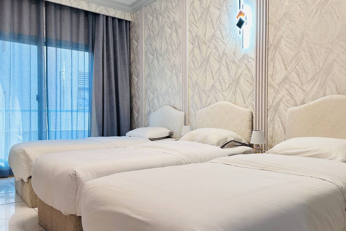 A hotel room with two beds, a large window with curtains, and a marble-patterned wall.