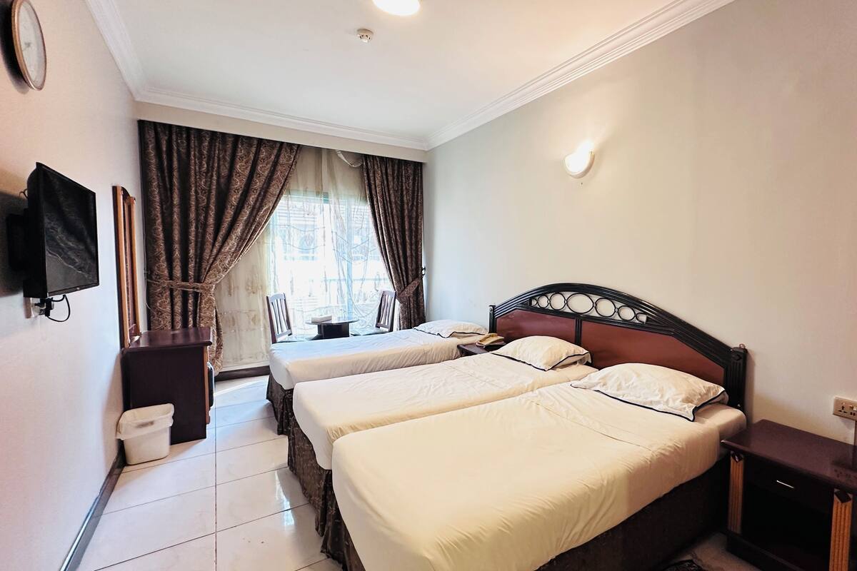 A hotel room with two beds, a television, a window with curtains, and a small table.