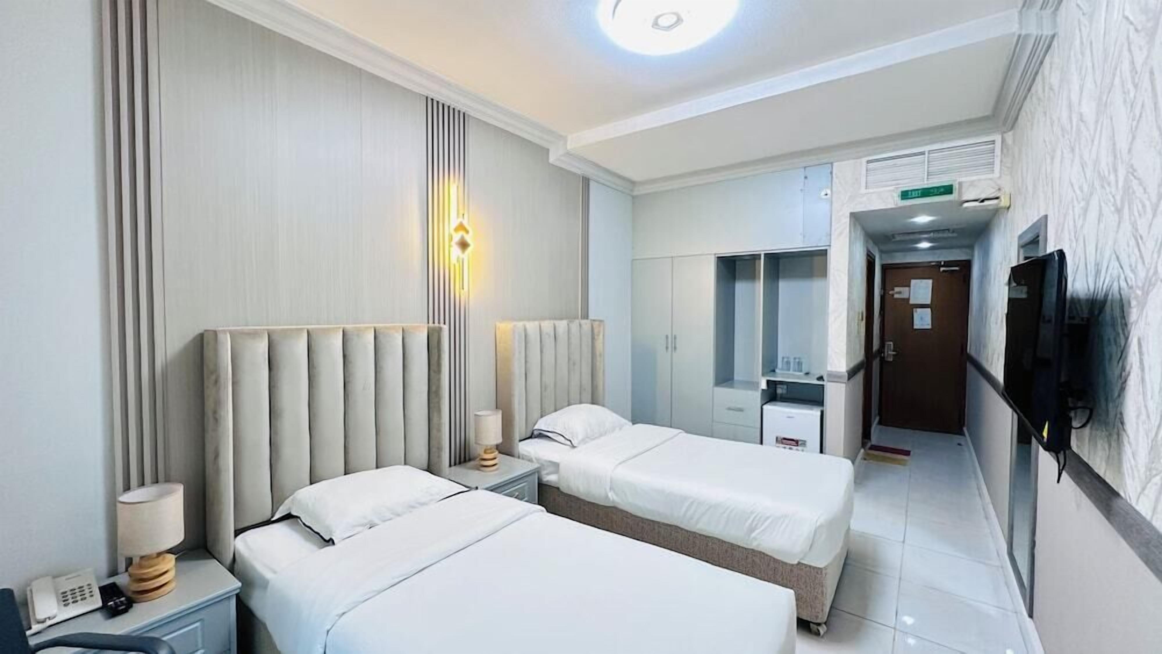 A hotel room with two beds, a bedside table with a lamp, a telephone, a wardrobe, and a television mounted on the wall.
