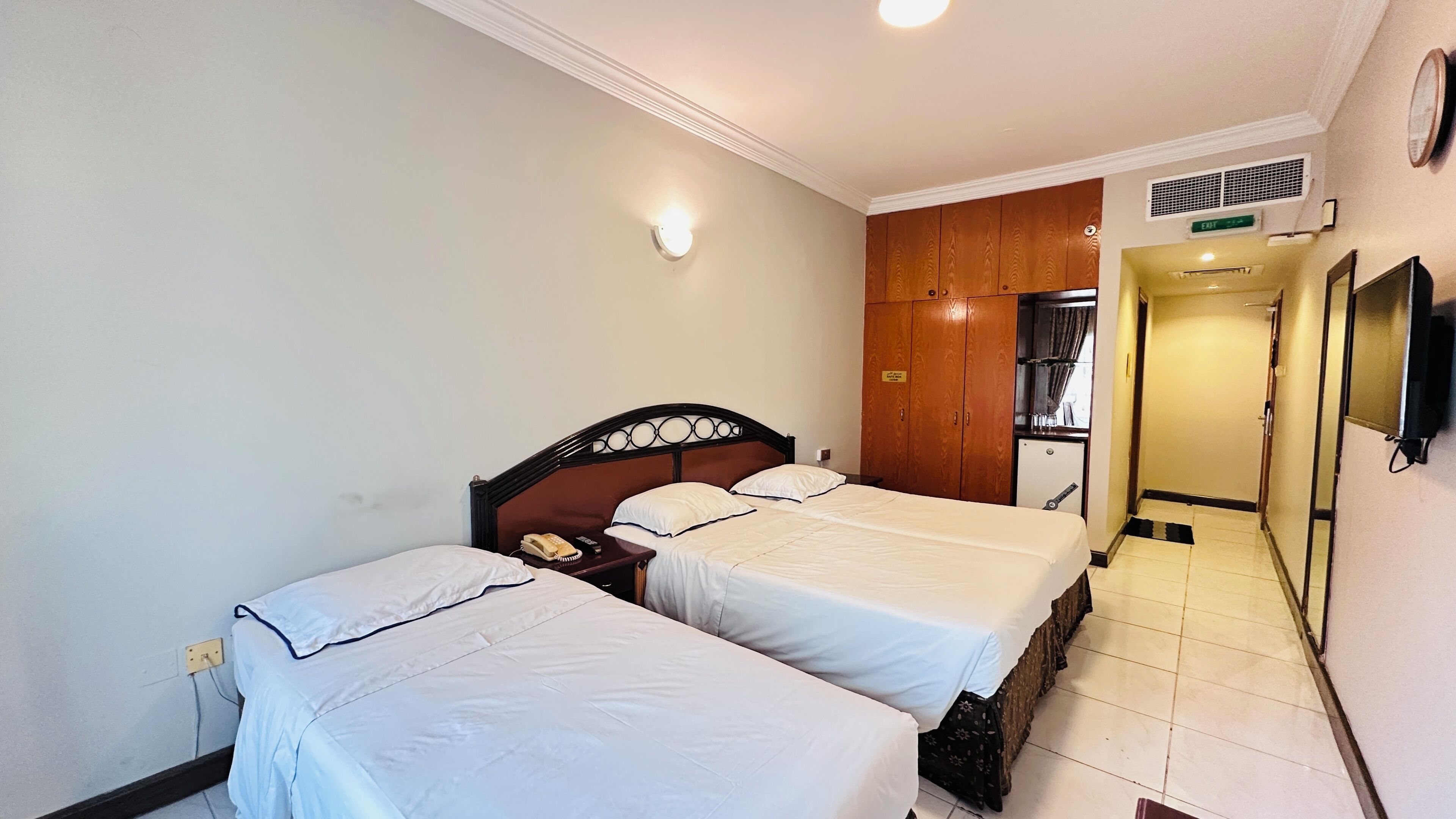 Ein Hotelzimmer mit zwei Betten, einem Nachttelefon, einem kleinen Kühlschrank und einem Spiegel an der Wand.