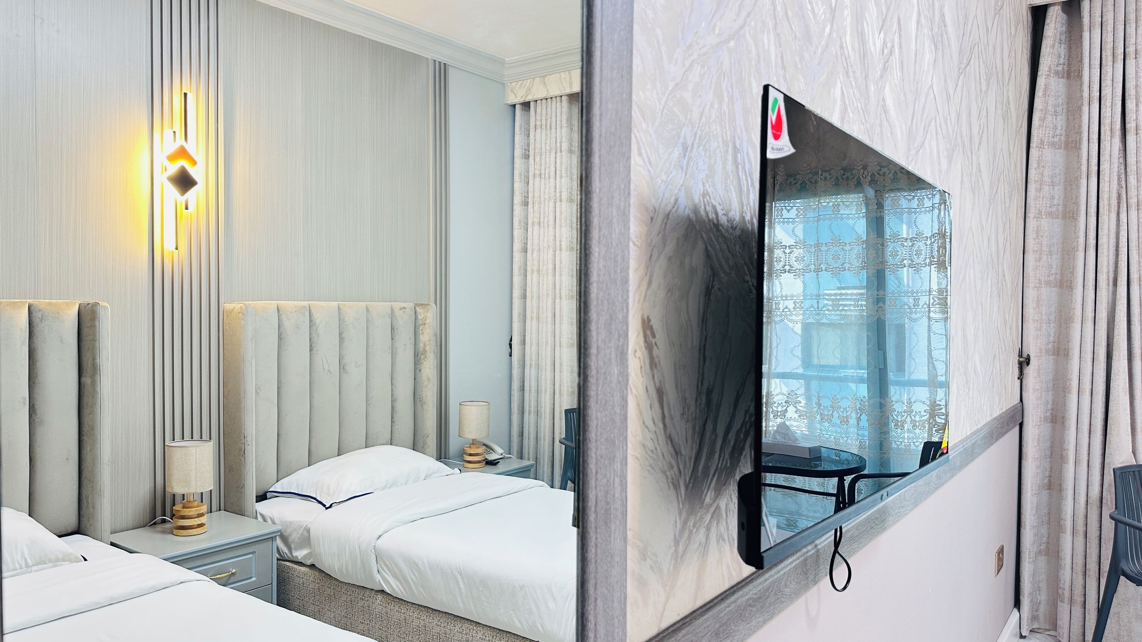 Una camera d'albergo con un letto grande, comodini con lampade, una TV a parete e una finestra vista edificio.