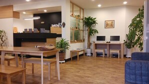 A modern guest house interior with a wooden reception desk, two computer stations, a fireplace, and several potted plants. - Sokcho & Guesthouse (Sokcho)