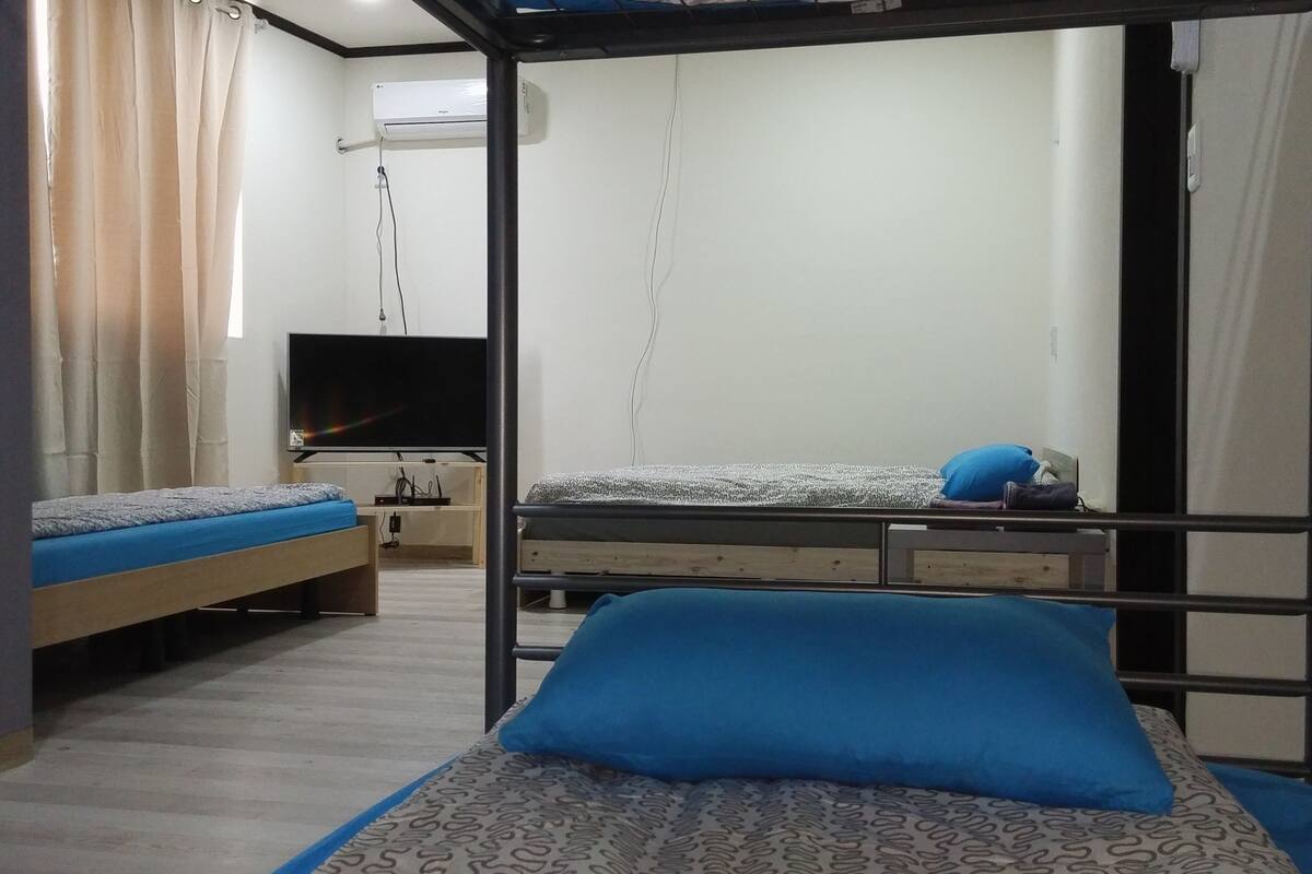A bunk bed room with a television, a desk, and a window with curtains.