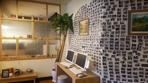 A room with a wooden desk, two computer monitors, a keyboard, and a mouse. There is a shelf with small figurines and a plant. The wall is covered with numerous black and white photographs. - Sokcho & Guesthouse (Sokcho)