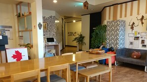 A cozy room with a wooden table and chairs, a couch, and a wall decorated with photos and a geometric pattern. - Sokcho & Guesthouse (Sokcho)