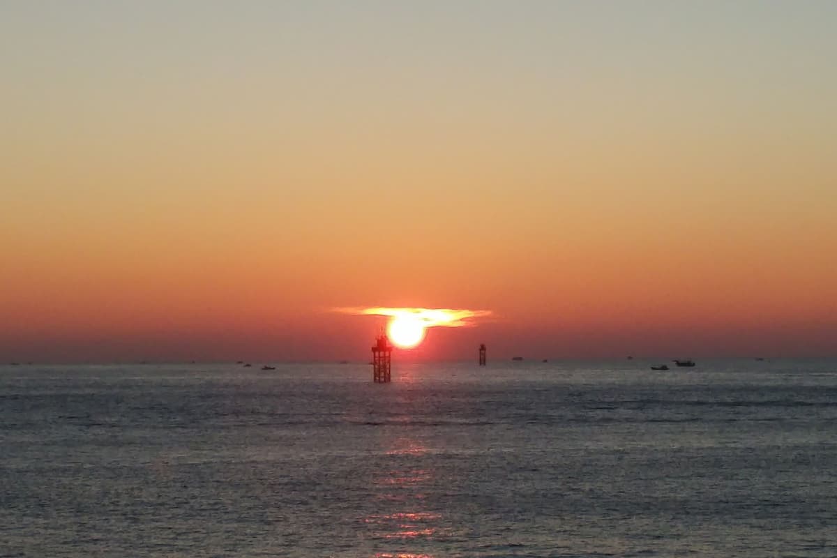 A sunset over a calm sea with a distant tower structure.