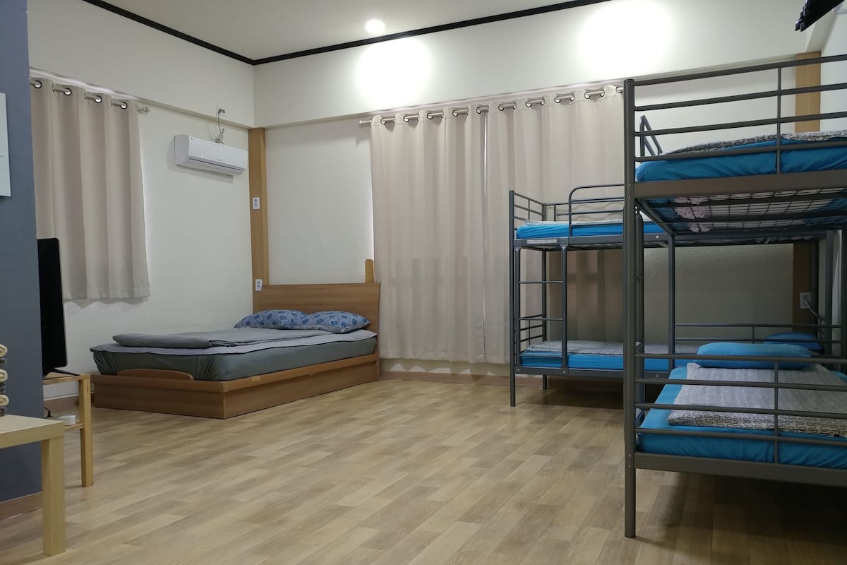 A dormitory room with a bunk bed, a single bed, a desk, and a TV.