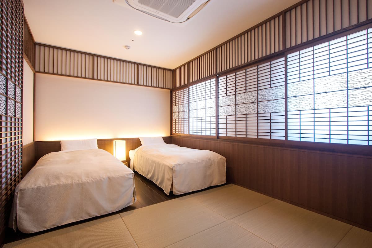 A hotel room with two beds, a large window with a view, and a traditional Japanese-style wall.
