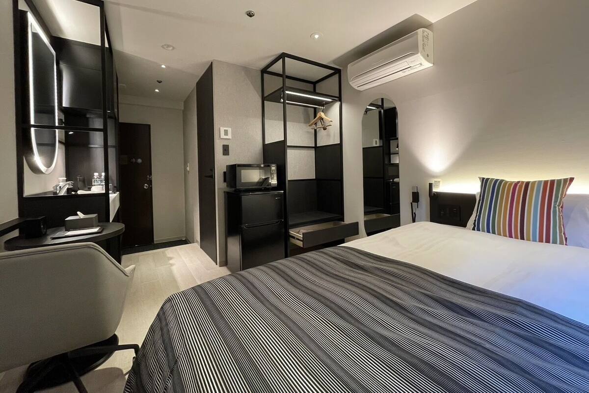 A modern hotel room with a bed, a desk, a mirror, and a wardrobe.