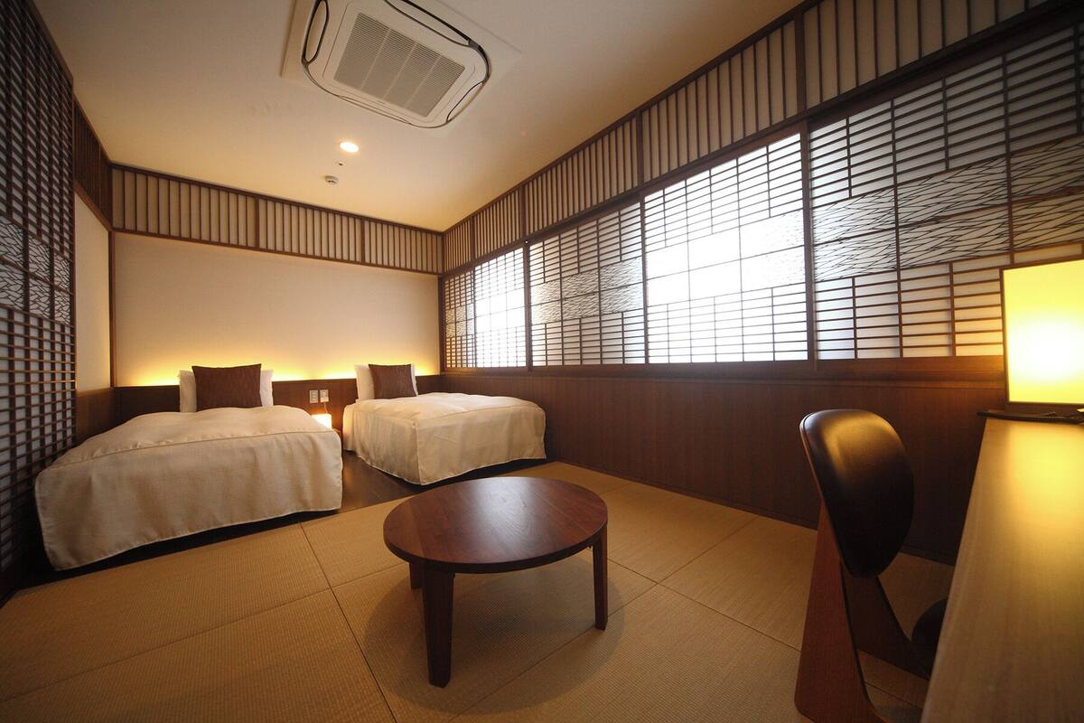 A hotel room with two beds, a round table, and a chair.