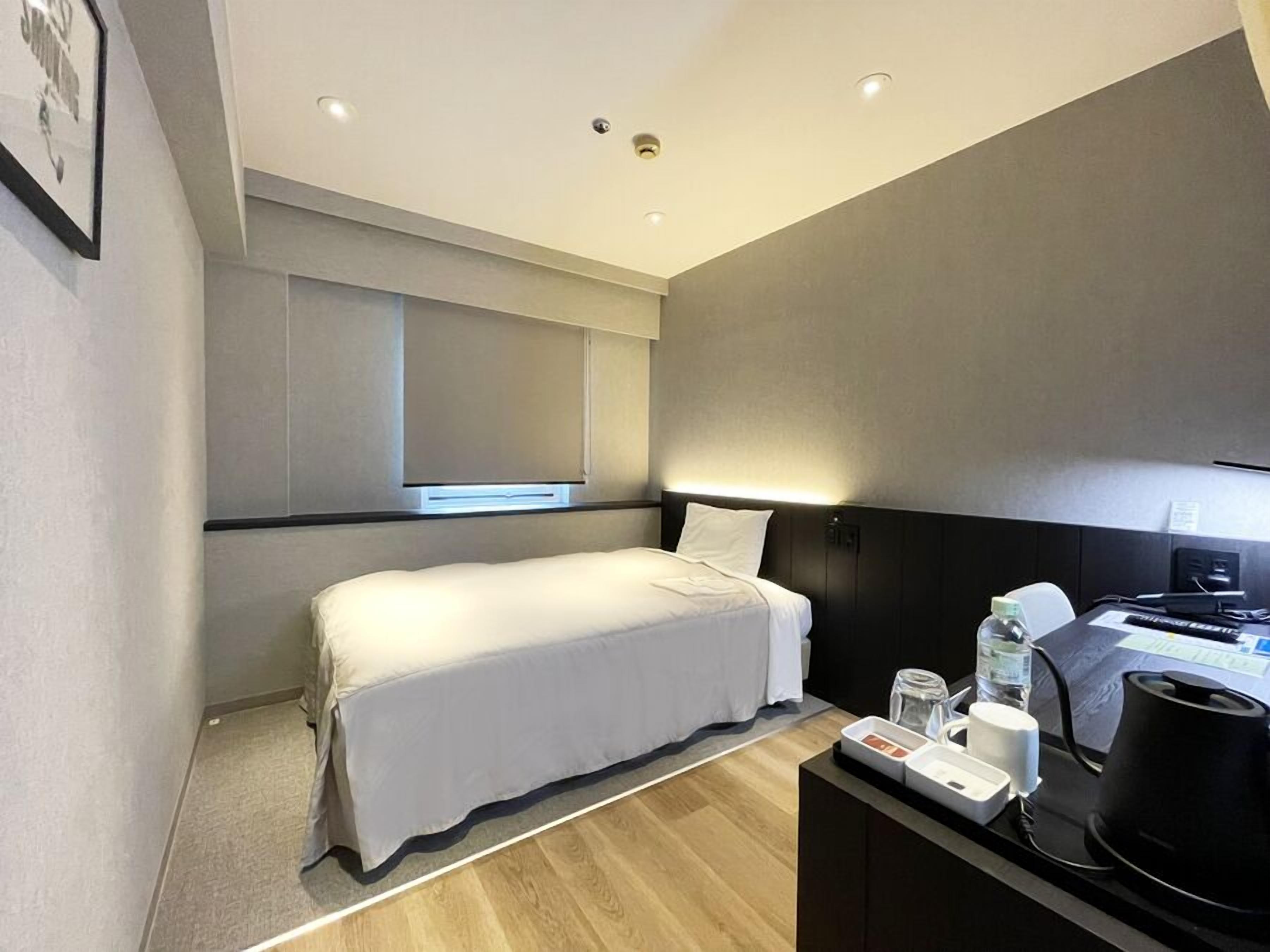 A modern hotel room with a bed, bedside table, and a desk with a computer and coffee maker.