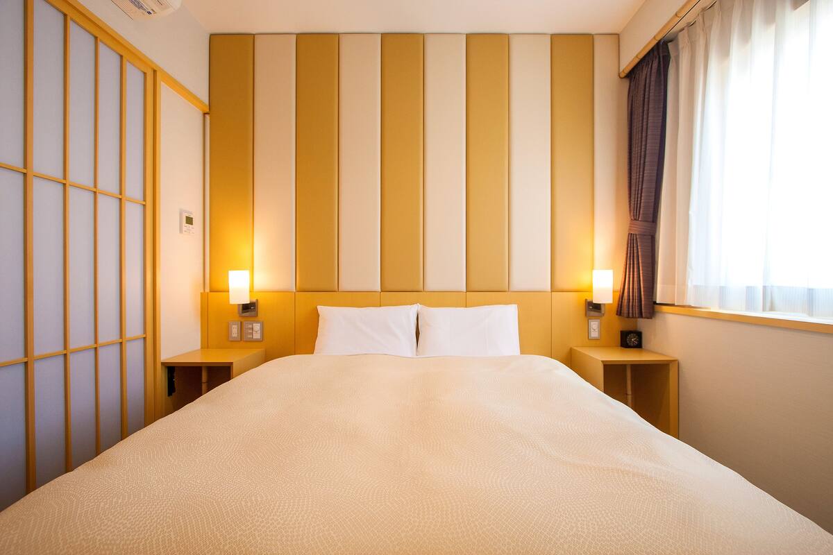 A hotel room with a large bed, two bedside tables with lamps, a wall with vertical stripes, and a window with curtains.