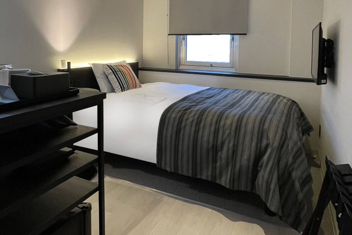 A modern hotel room with a bed, a desk, and a window.