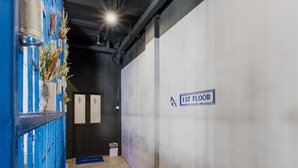 A hallway with a sign indicating the 1st floor, a blue wall with decorative elements, and a trash bin. - Loftel Station Hostel (Bangkok)