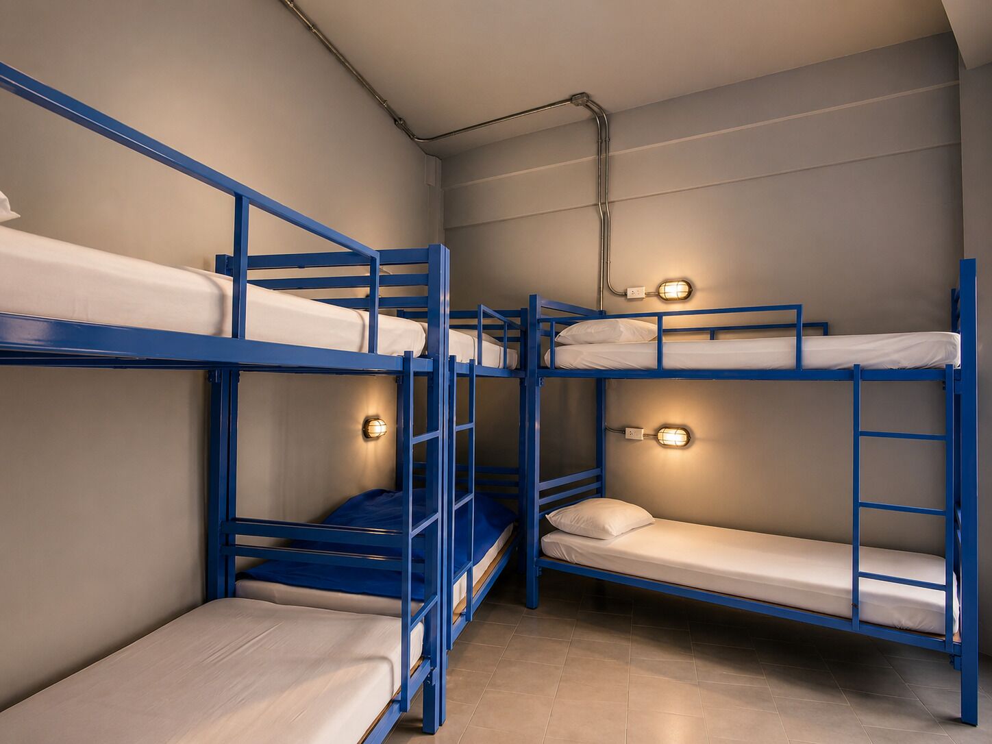 Habitación con literas de estructura azul, una lámpara en cada litera y un enchufe visible en la pared.