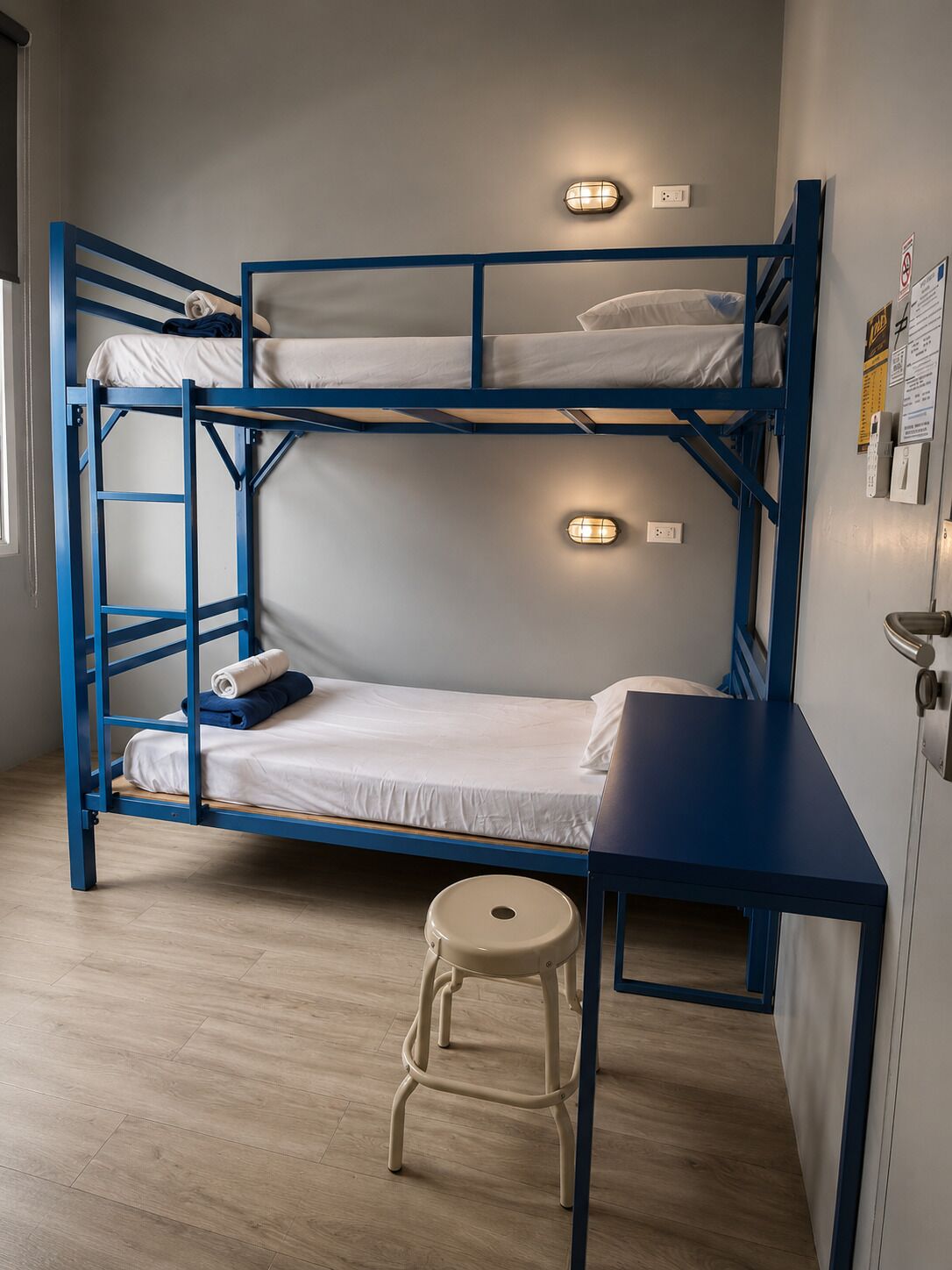 A bunk bed room with a desk and stool, light fixtures, and a window.