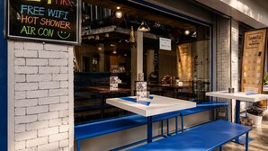 A restaurant with outdoor seating, a chalkboard sign advertising free wifi, hot showers, and air conditioning. - Loftel Station Hostel (Bangkok)