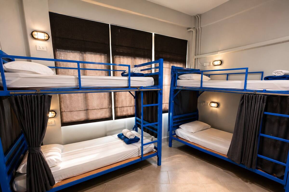 A bunk bed room with two beds, a window with curtains, and wall-mounted lights.