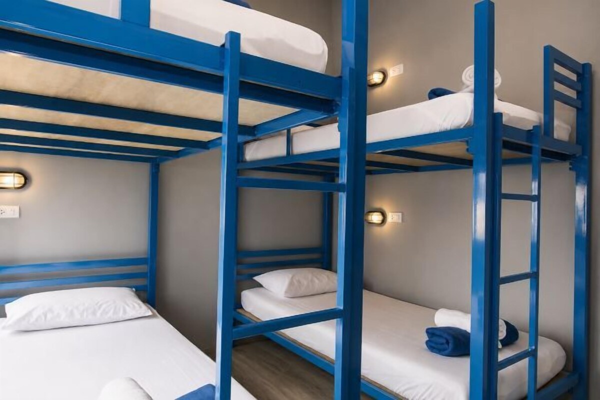 Quarto com beliche, escada, roupa de cama branca e luzes fixadas na parede.