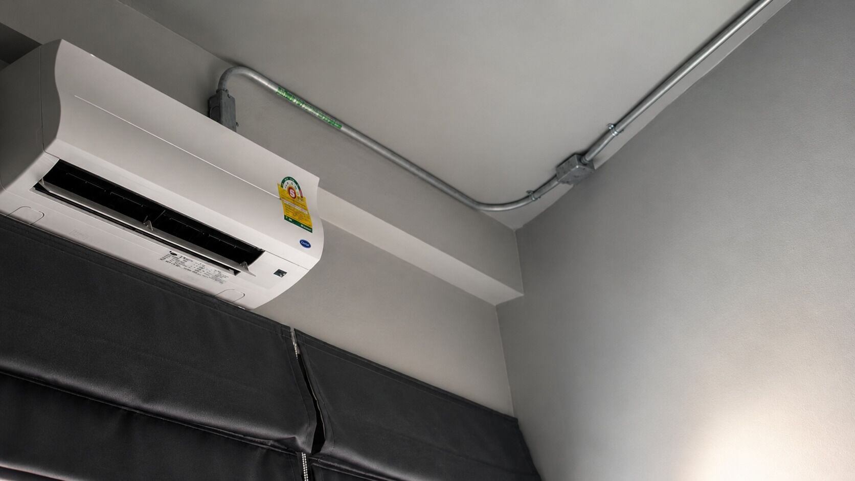 A room with a white ceiling, a white air conditioning unit, and a grey wall.