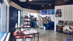 A cafe interior with tables, a counter, and a menu board. - Loftel Station Hostel (Bangkok)