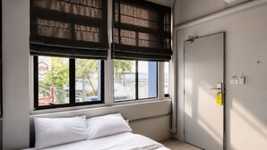 A bedroom with a bed, a window with blinds, a door, and a thermostat. - Loftel Station Hostel (Bangkok)