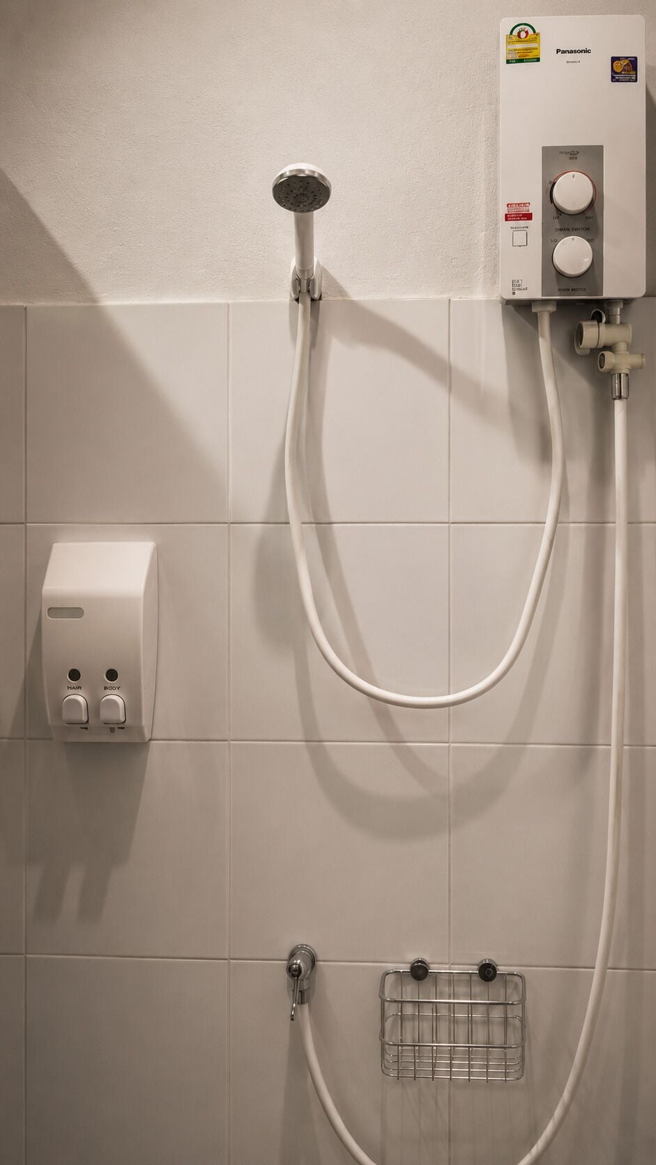 A shower with a handheld showerhead, a control panel, and a soap dispenser.