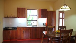 A kitchen with wooden cabinets, a dining table with chairs, a window with a view, and a hanging light fixture.