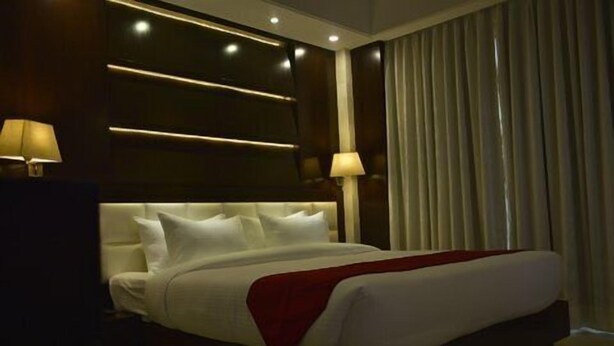 Ein Hotelzimmer mit einem großen Bett, zwei Nachttischlampen, einem dunklen Kopfteil und einem Fenster mit Vorhängen.