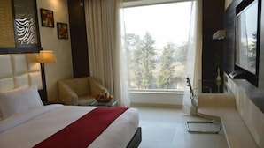 Ein Hotelzimmer mit Bett, Schreibtisch, Stuhl, Fernseher und Fenster mit Blick auf Bäume.