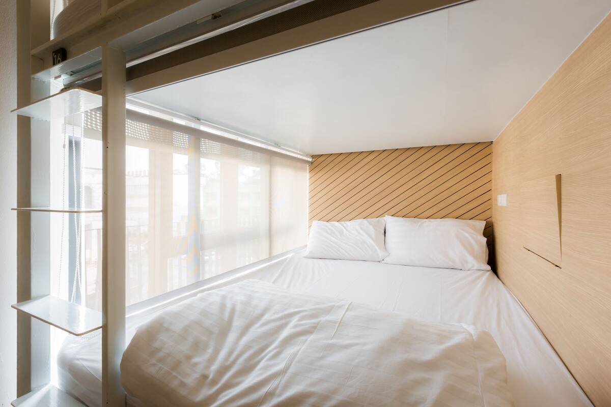 A modern bedroom with a large bed, a wooden headboard, and a window with blinds.