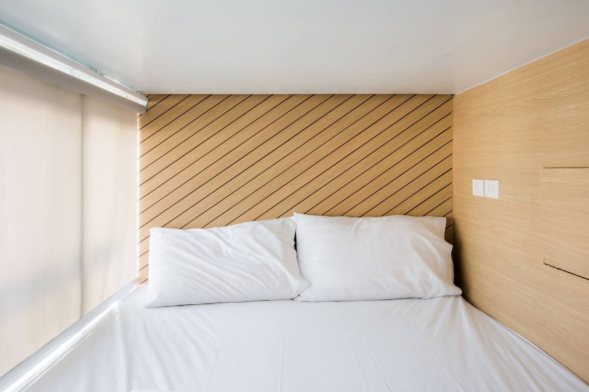 A small, neatly made bed with white linens in a room with wooden paneling and a sloped ceiling.