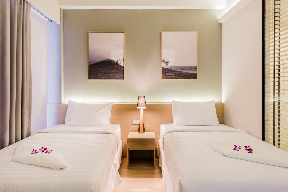 A hotel room with two beds, a nightstand with a lamp, and two framed pictures on the wall.