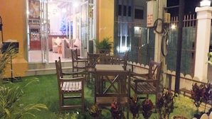 An outdoor patio with wooden furniture, a glass door entrance, and a fenced area with plants. - Avalon Residence (Savannakhet)