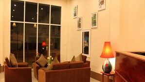 A modern living room with brown sofas, a wooden reception desk, and large windows. - Avalon Residence (Savannakhet)