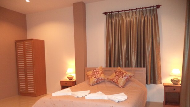 A neatly made bed with pillows, a nightstand with a lamp, and a wardrobe. - Avalon Residence (Savannakhet)