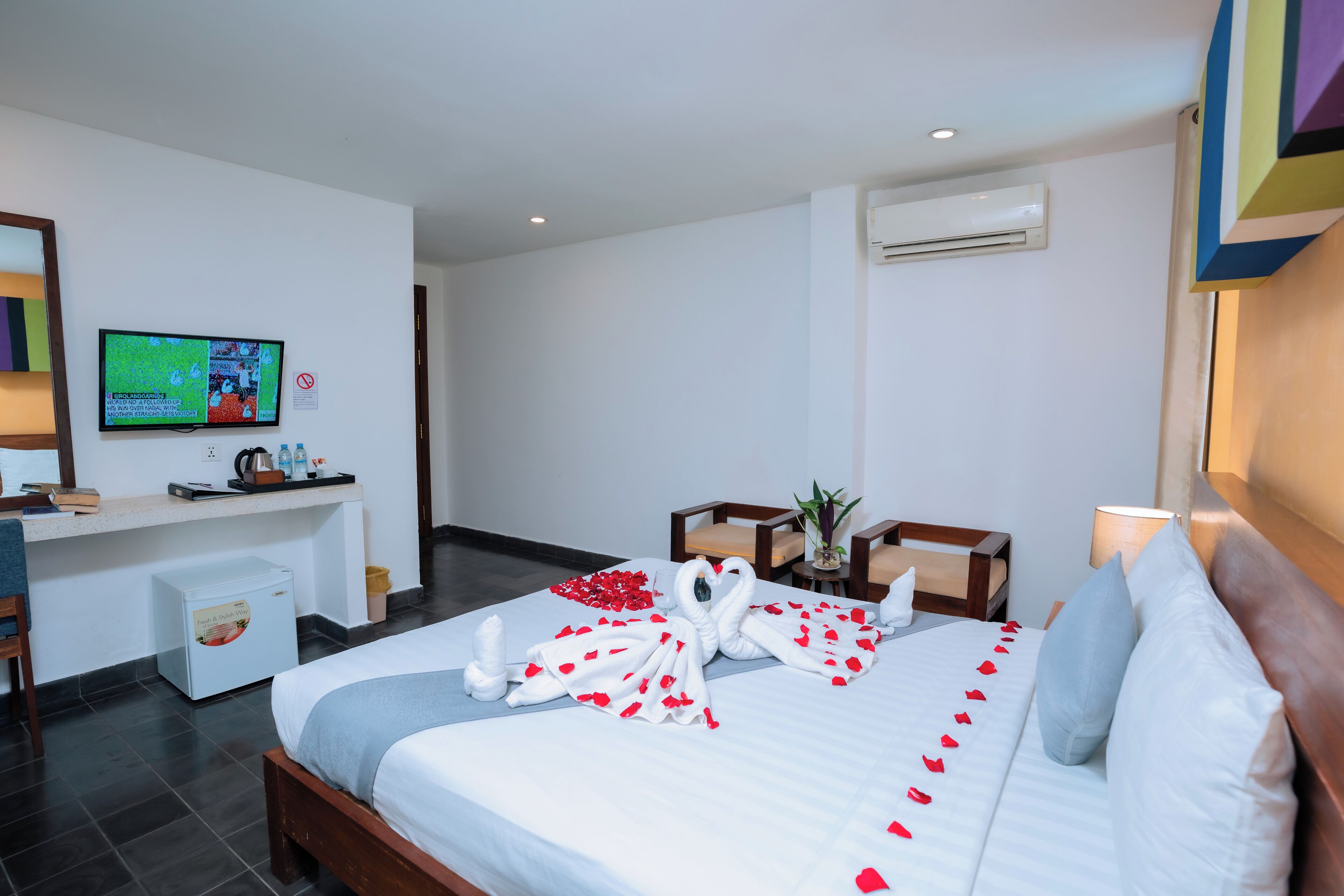 A hotel room with a bed, a desk, a television, and a small refrigerator.