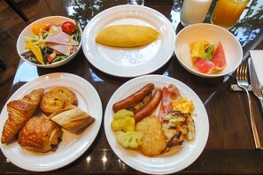 Una mesa de desayuno con platos de comida, incluyendo croissants, salchichas y una ensalada.