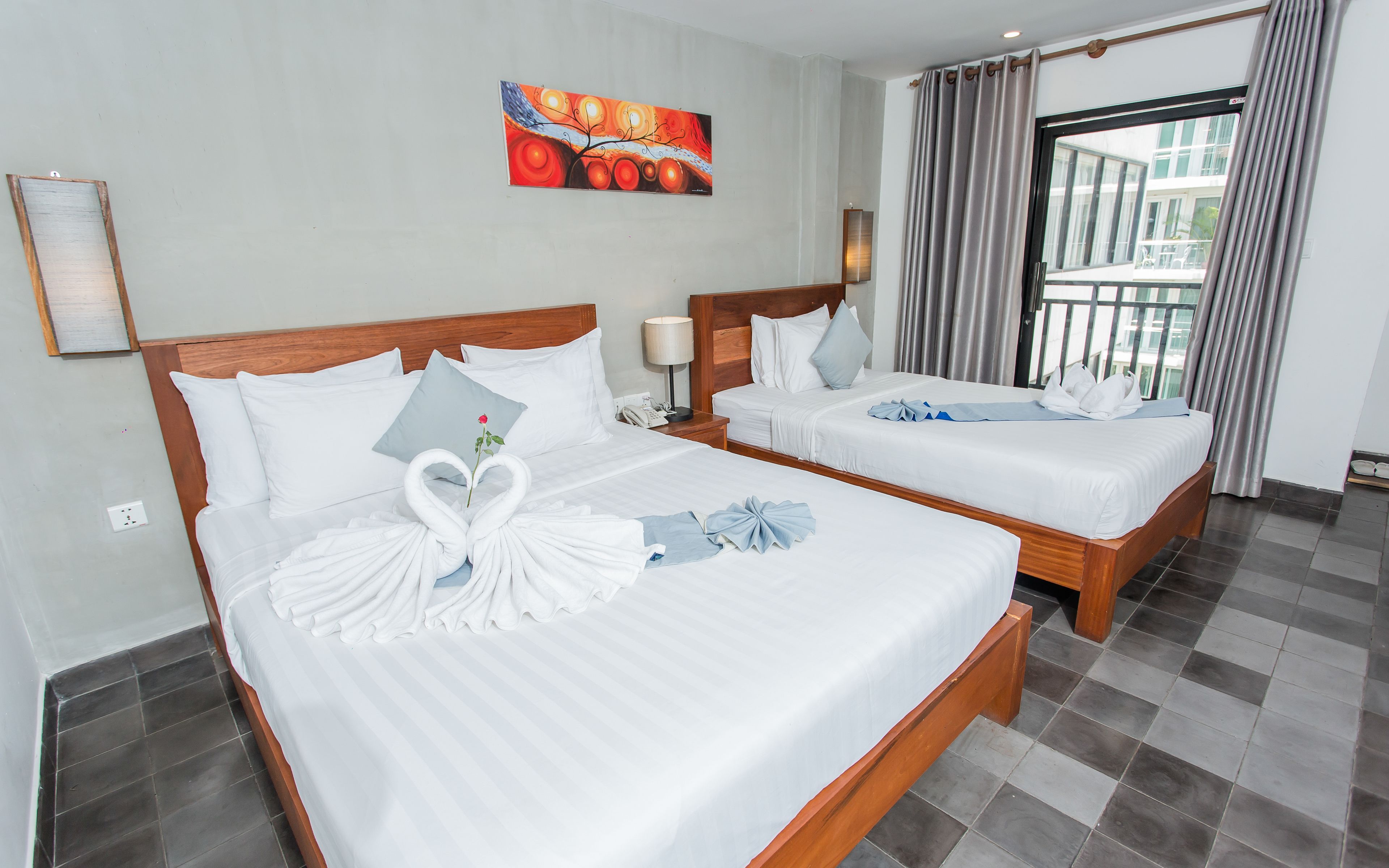 A hotel room with two beds, each with white linens and decorative towels. There is a painting on the wall and a window with curtains.