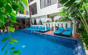 Zona de piscina con sillas reclinables azules y una piscina con baldosas.