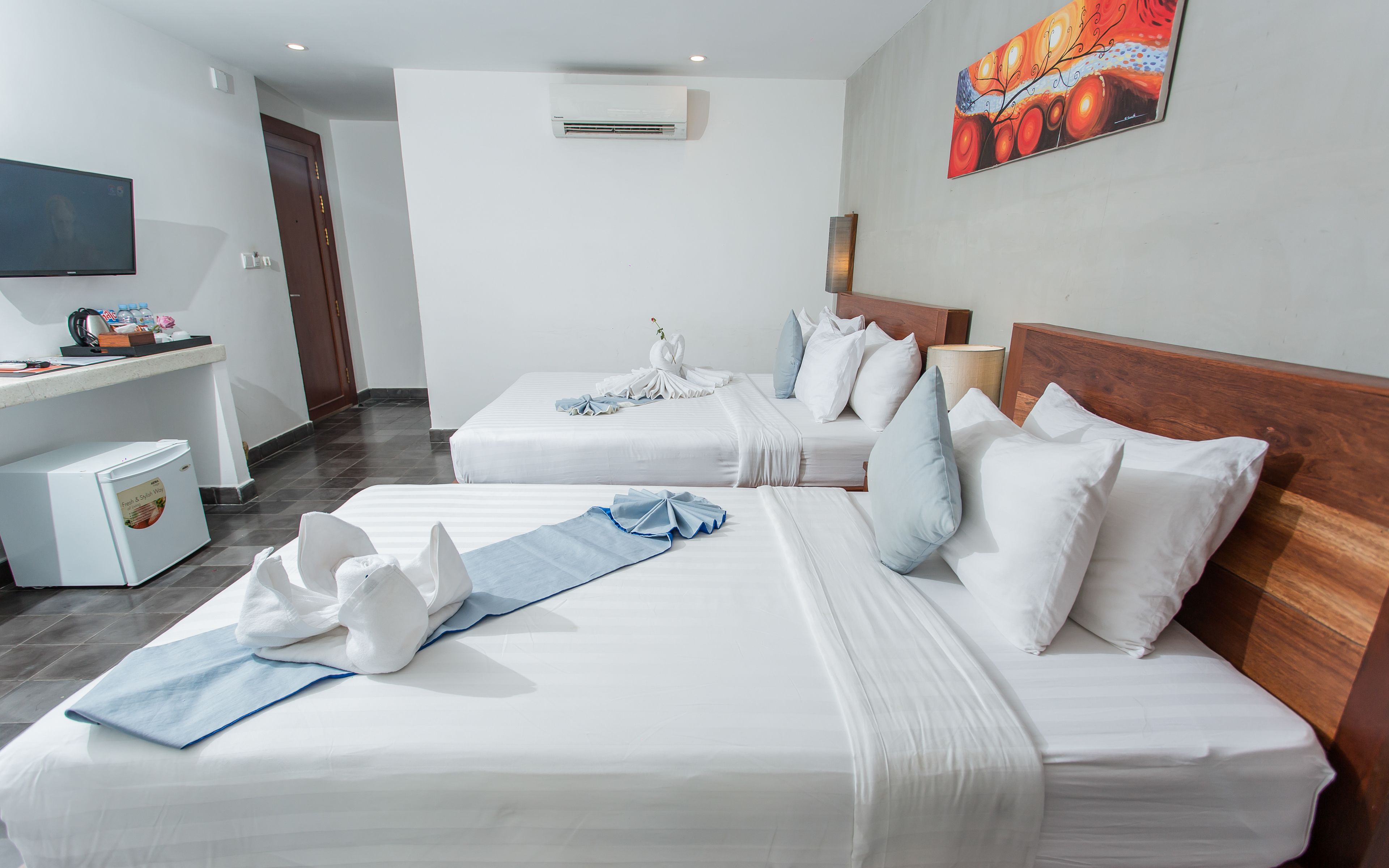 A hotel room with two beds, a desk, a television, and an air conditioning unit.