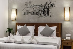 Una cama bien hecha con tablero de madera, dos almohadas, una mesita de noche con un teléfono y una obra de arte que representa una escena urbana.