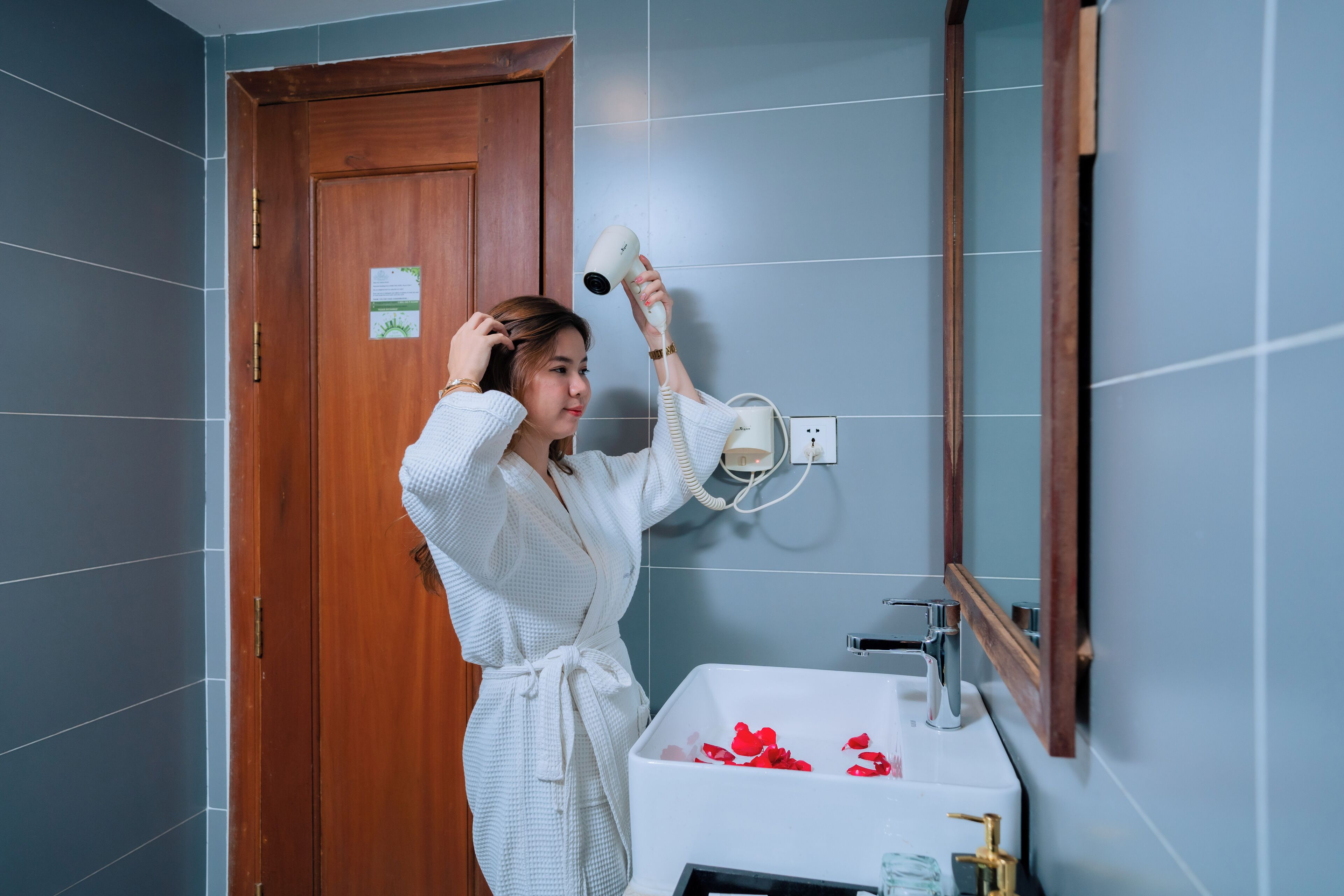 Une salle de bain avec une porte en bois, un lavabo blanc orné de pétales de roses rouges et un miroir.